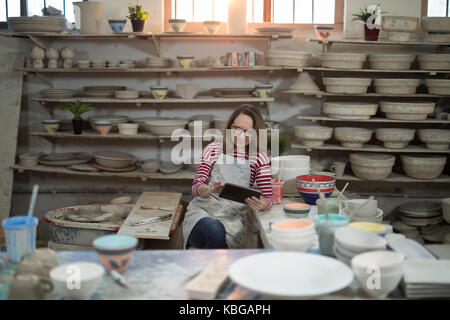 Potter femelle using digital tablet in atelier de poterie