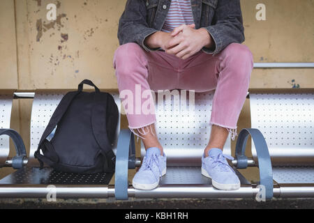 La section basse de l'homme assis sur un banc à la gare Banque D'Images