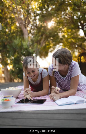 Petite-fille et grand-mère souriante using digital tablet in garden sur une journée ensoleillée Banque D'Images