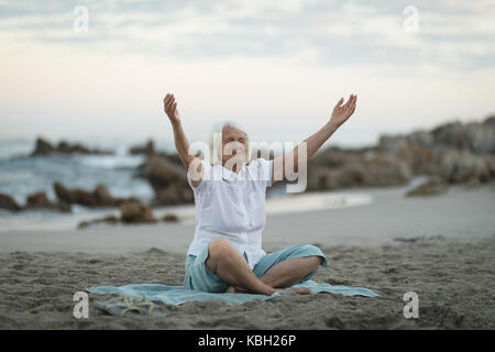 Senior woman with her hands raised assis sur la plage Banque D'Images