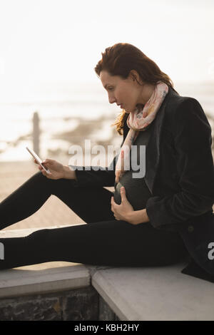 Femme enceinte assis près de la plage sur une journée ensoleillée Banque D'Images
