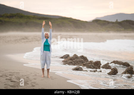 Healthy Senior woman exercise on beach pendant le crépuscule Banque D'Images