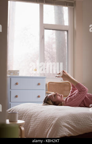 Vue latérale du jeune femme détendue avec phone sur le lit chez lui Banque D'Images