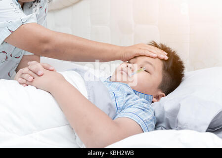 Sick boy avec thermomètre portant sur le lit et prendre la température. La main de la mère à l'enfant malade avec de la fièvre et la maladie au lit Banque D'Images