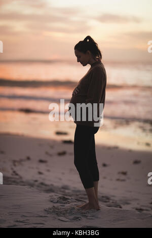 Silhouette de femme enceinte, debout sur la plage au crépuscule Banque D'Images
