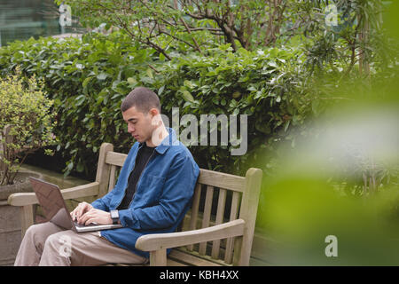 Homme assis sur le banc et using laptop in park Banque D'Images