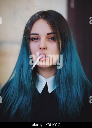 Emo girl cigarette. jeune étudiant ou l'élève avec les cheveux teints de couleur bleu, hat, lentilles,piercing,oreilles de tunnels et de coiffure inhabituelle se dresse sur bla Banque D'Images