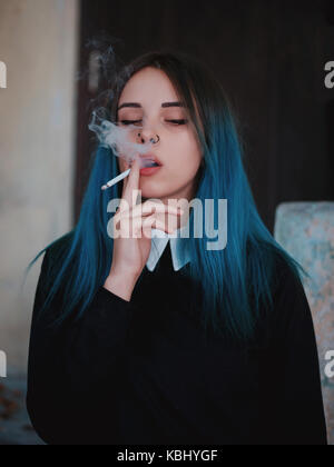 Emo girl cigarette. jeune étudiant ou l'élève avec les cheveux teints de couleur bleu, hat, lentilles,piercing,oreilles de tunnels et de coiffure inhabituelle se dresse sur bla Banque D'Images