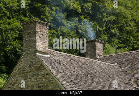 La fumée s'élevant à partir de la cheminée de pierre construite ferme avec arbres en arrière-plan. St Fagans, Cardiff, Royaume-Uni Banque D'Images