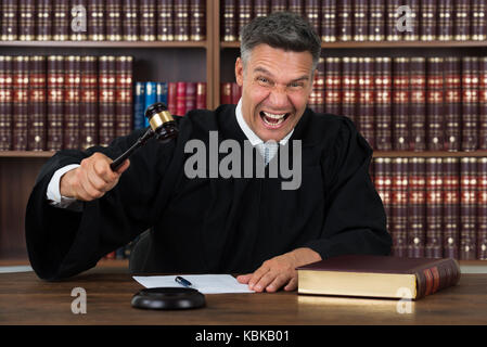 Portrait of mature en colère frappant son marteau juge à table dans la salle d'audience Banque D'Images