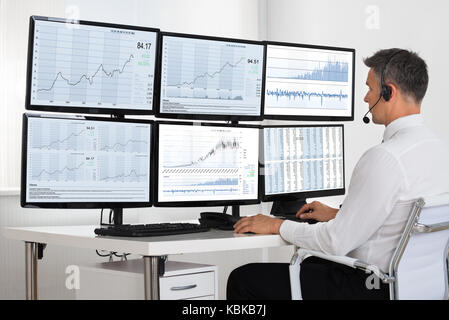 Vue latérale du courtier en bourse à la recherche à des graphiques sur plusieurs écrans dans office Banque D'Images