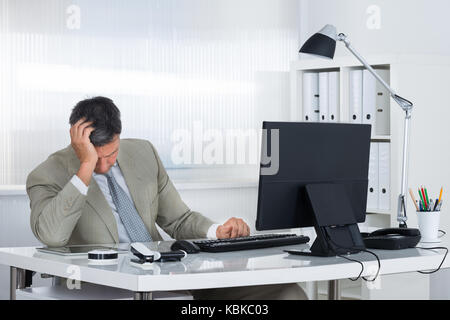 Fatigué businessman leaning head à portée de main lorsque sitting at desk in office Banque D'Images