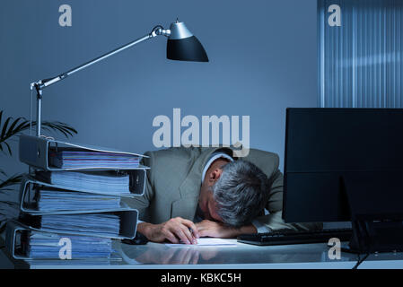 Épuisé businessman leaning head sur 24 par classeurs tout en travaillant à la fin de l'office de tourisme Banque D'Images