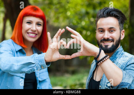 Couple d'amoureux formant un cœur avec leurs mains dans un parc Banque D'Images