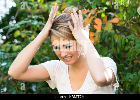 Jeune femme frustrée avec les mains sur la tête contre des plantes Banque D'Images