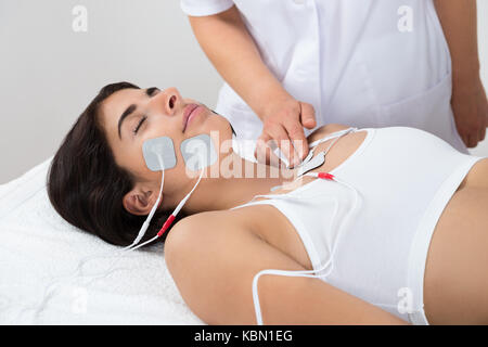 Donnant à la thérapie thérapeute électrodes young woman lying on bed Banque D'Images