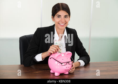 Young businesswoman insertion à 24 Billets in piggybank Banque D'Images