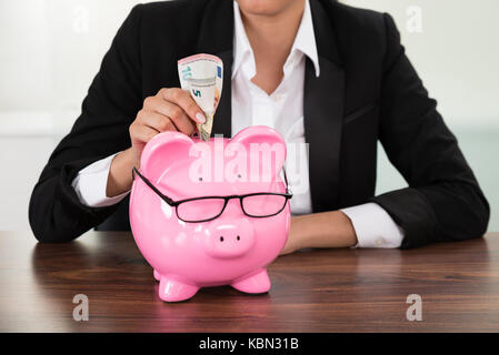 Young businesswoman insertion à 24 Billets in piggybank Banque D'Images
