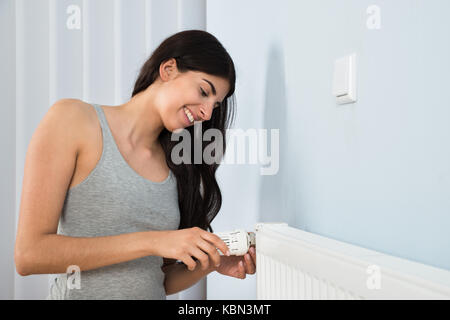 Jeune femme heureuse thermostat de réglage sur le radiateur à la maison Banque D'Images