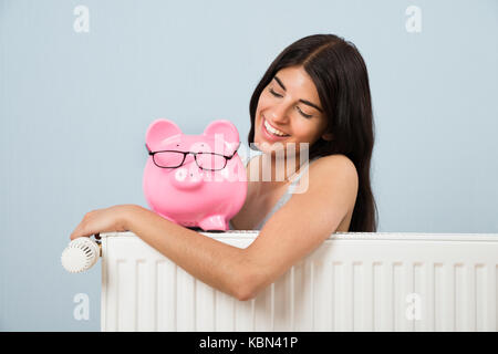 Young woman leaning on radiateur avec pink piggybank à la maison Banque D'Images