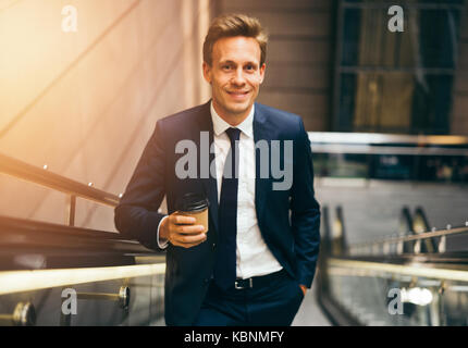 Confident young businessman smiling en buvant un café et d'un escalator dans une station de métro au cours de son trajet du matin Banque D'Images