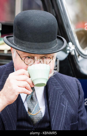 En Angleterre, Chatham. Un homme âgé, moustache grise et des lunettes, vêtu de noir chapeau melon. En face, dans les yeux. Vers les années 1940 de la reconstitution médiévale. Boire une tasse de thé. Banque D'Images