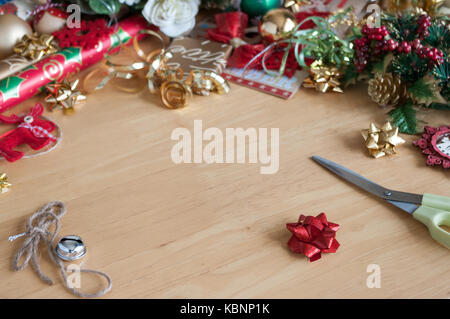 L'emballage de cadeaux et décorations de noël formant une bordure sur fond de bois clair. Banque D'Images