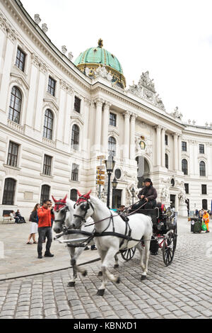 Célèbre appelé calèche fiaker passe par le Palais de la Hofburg à Vienne à Michaelerplatz avec les touristes et les gens. Banque D'Images