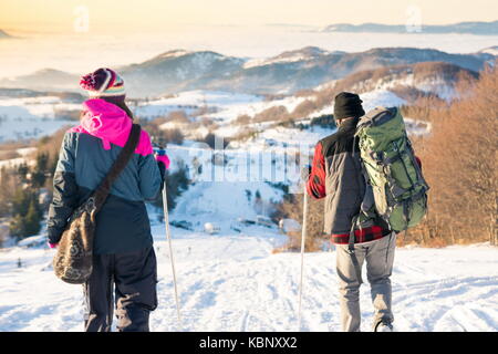 Couple marchant dans la montagne enneigée à l'heure du coucher du soleil romantique Banque D'Images