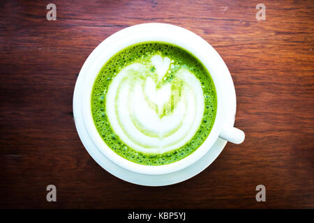 Thé vert matcha latte avec forme de coeur latte art en coupe blanche sur table en bois. vue d'en haut. Banque D'Images