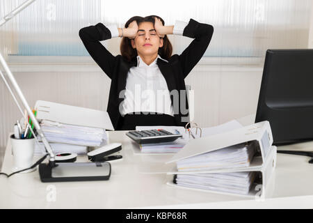 Femme assise se raidit comptable with head in hands at desk in office Banque D'Images