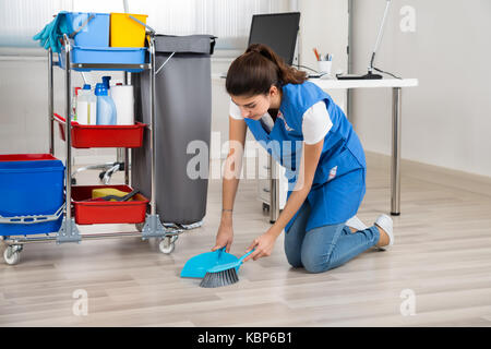 Longueur totale de jeunes femmes balayant nettoyant parquet in office Banque D'Images