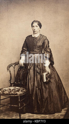 Archive américaine studio monochrome portrait photographique de femme plus âgée avec stern expression portant une robe sombre debout à côté d'une chaise de salle à manger meubles capitonnés, nommée Matilda Gage, prises à la fin du 19e siècle par Webster et Battey Photographes, Binghamton, NY, USA Banque D'Images