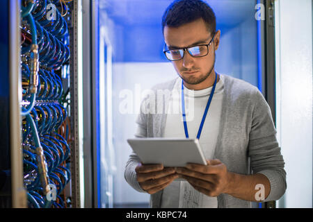 Portrait of young woman standing by cabinet de serveur tout en travaillant avec des supercalculateur en lumière bleue Banque D'Images