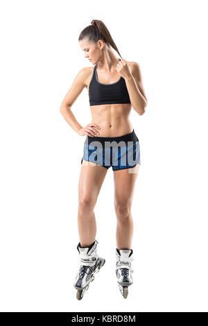 Jeune femme sportive fit confiance à patins à toucher à la queue de cheval vers le bas. pleine longueur du corps portrait isolé sur fond blanc studio. Banque D'Images