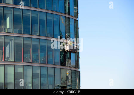 Hommes utilisant un palan de berceau sur 2 plus London Riverside bâtiment de façade de fenêtre de verre, Londres, Royaume-Uni. Ouvriers travaillant en hauteur sur un bâtiment de grande hauteur Banque D'Images