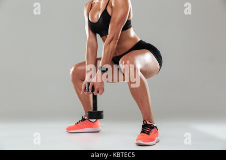 Portrait d'un athlète woman doing squats d'haltères avec un fond gris plus isolés Banque D'Images