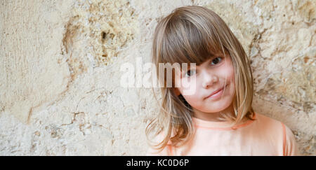 Smiling caucasian légèrement petite fille, close-up portrait en extérieur sur mur de pierre Banque D'Images