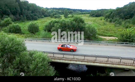 Relevé aérien de la voiture se déplace sur la serpentine. flying over red cabriolet dur la rue.Vue aérienne de la voiture rouge qui passe sur le pont. Le trafic sur le pont. Voiture rouge. Banque D'Images