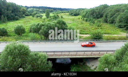 Relevé aérien de la voiture se déplace sur la serpentine. flying over red cabriolet dur la rue.Vue aérienne de la voiture rouge qui passe sur le pont. Le trafic sur le pont. Voiture rouge. Banque D'Images