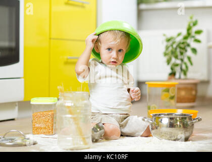 Bébé garçon enfant assis sur le plancher de la cuisine et jouer avec la farine. Banque D'Images