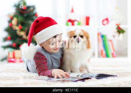 Petit garçon de lire un livre et le chien couché à l'arbre de Noël Banque D'Images