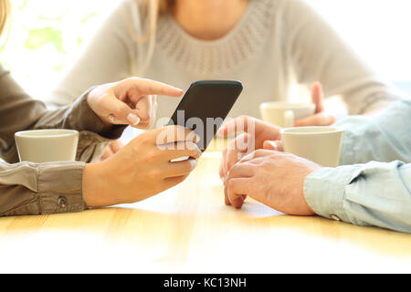 Close up de trois amis mains regardant le contenu multimédia dans un téléphone intelligent assis dans une table d'un bar ou d'une chambre Banque D'Images
