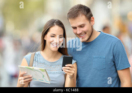 Vue de face d'un couple d'heureux touristes emplacement recherche sur la ligne avec un téléphone et carte sur la rue Banque D'Images