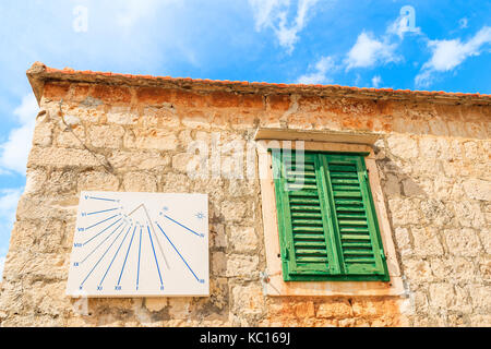 Ville de Postira, Croatie - 7 SEP 2017 : horloge du soleil et vert fenêtre sur façade de maison ancienne en pierre dans la ville de Supetar, île de Brac, Croatie. Banque D'Images