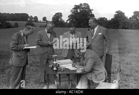 Années 1950, historiques, fumeurs de pipe, groupe d'hommes se tenir autour d'une table avec des trophées, tandis que l'un prend des notes et un autre homme assis à la table, England, UK. Banque D'Images