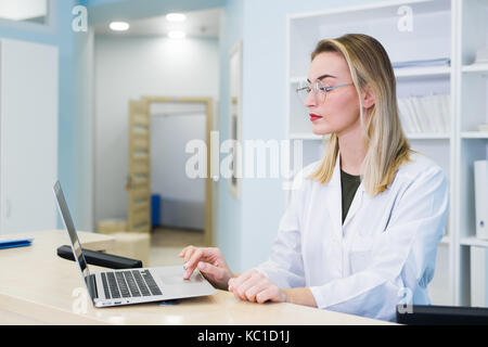 Médecin femme portant un maquis et travaillant à l'hôpital la réception, elle est l'écriture d'un rapport médical sur un presse-papiers et de la programmation des rendez-vous Banque D'Images