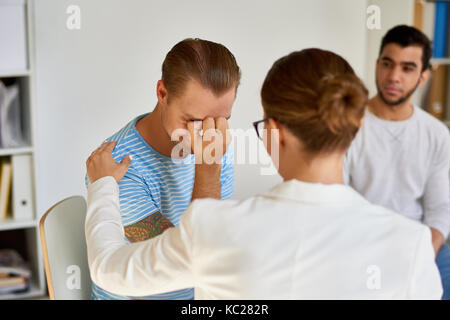 Portrait de jeune homme moderne de pleurer tout en partageant des problèmes avec femme psychiatre dans la thérapie de groupe session Banque D'Images