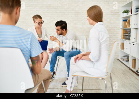 Portrait de jeune homme qui crie dans le groupe de soutien de problèmes de partage avec les autres participants et psychiatre en cercle Banque D'Images