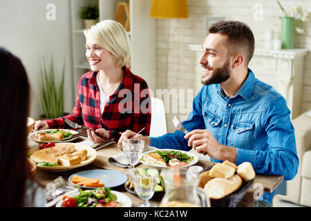 Portrait of happy young man and woman sitting at table avec de délicieux repas, bénéficiant d'un dîner de fête avec des amis à accueil rassemblement Banque D'Images